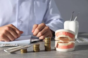 A dental professional's workspace with a model of dentures on display, alongside piles of coins and a calculator, symbolizing the financial planning aspect of denture services.