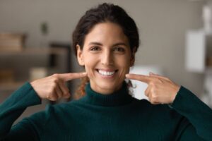 A cheerful woman in a teal sweater showcasing her healthy smile, representing the successful results of quality denture services.